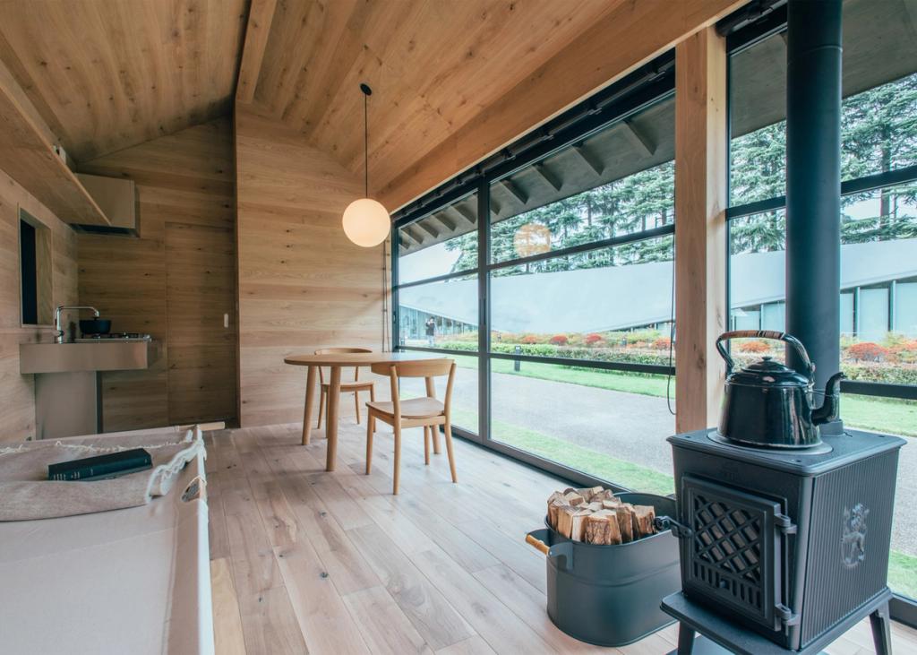 Interior of the MUJI Hut with timber cladding, a table, a cast-iron stove and a panoramic window