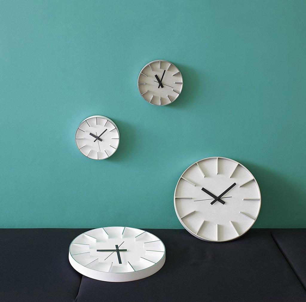 Four minimalist wall clocks with cut-out hour markers on a turquoise wall