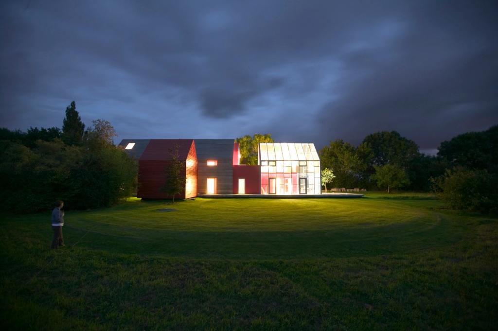 The dRMM Sliding House at night with an illuminated lawn and a lone figure