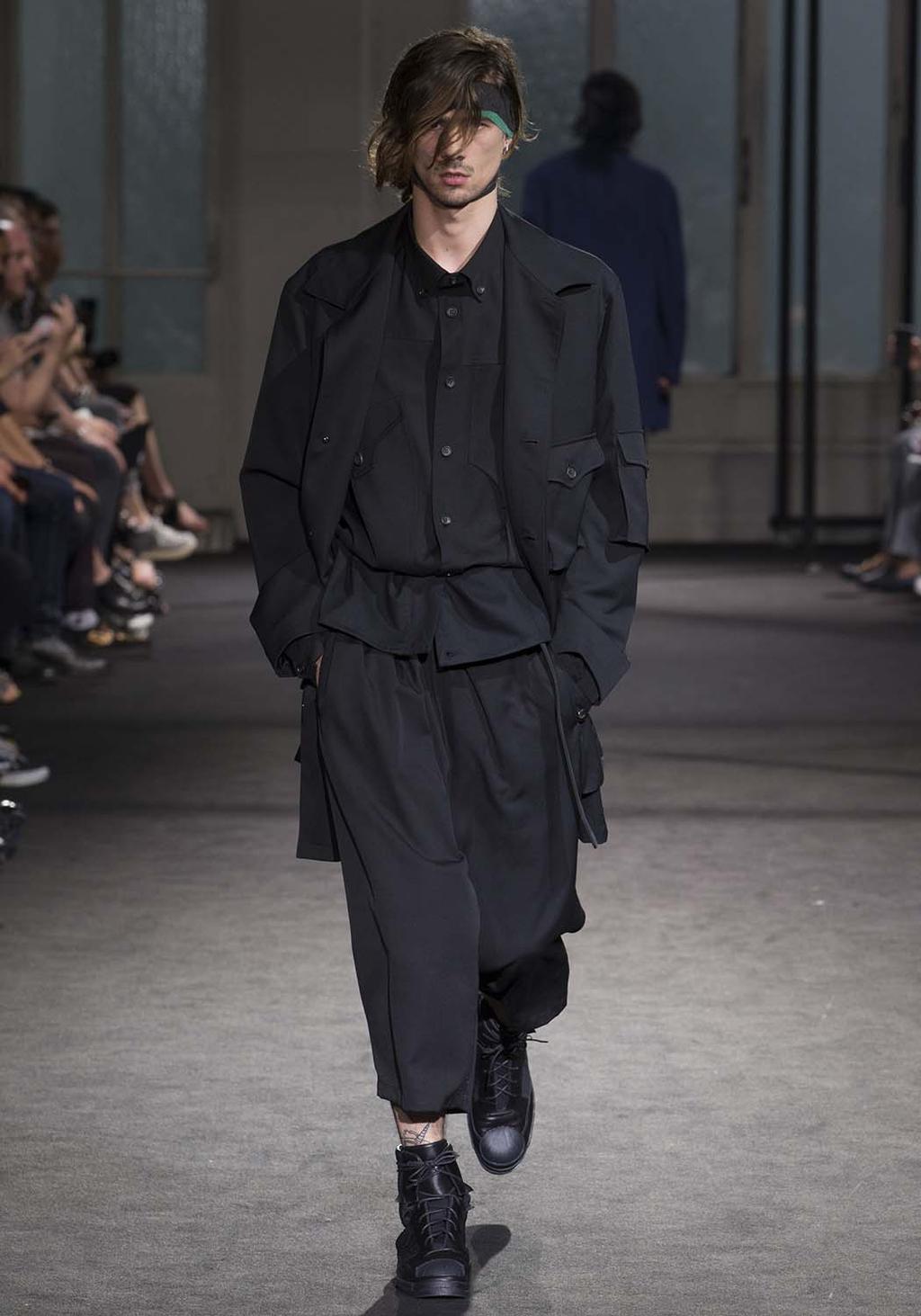 A man in a black jacket with pockets and wide trousers at a runway show