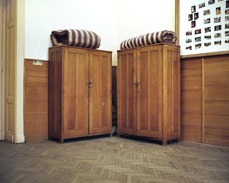Two wooden wardrobes with rolled striped mattresses on top, in a room with a parquet floor
