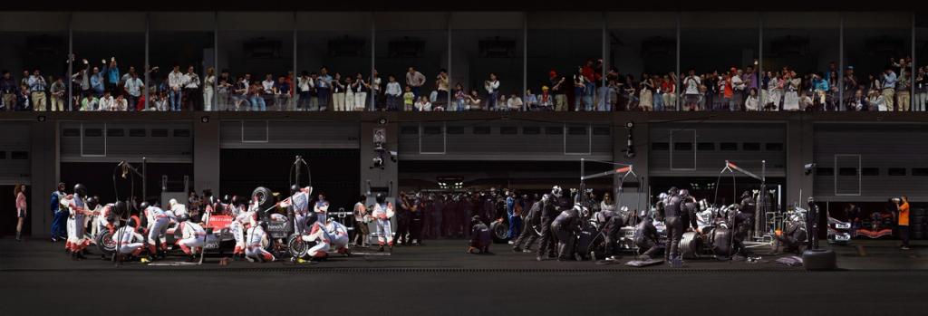 Formula 1 pit-stop panorama: mechanics beside the cars beneath a grandstand packed with spectators