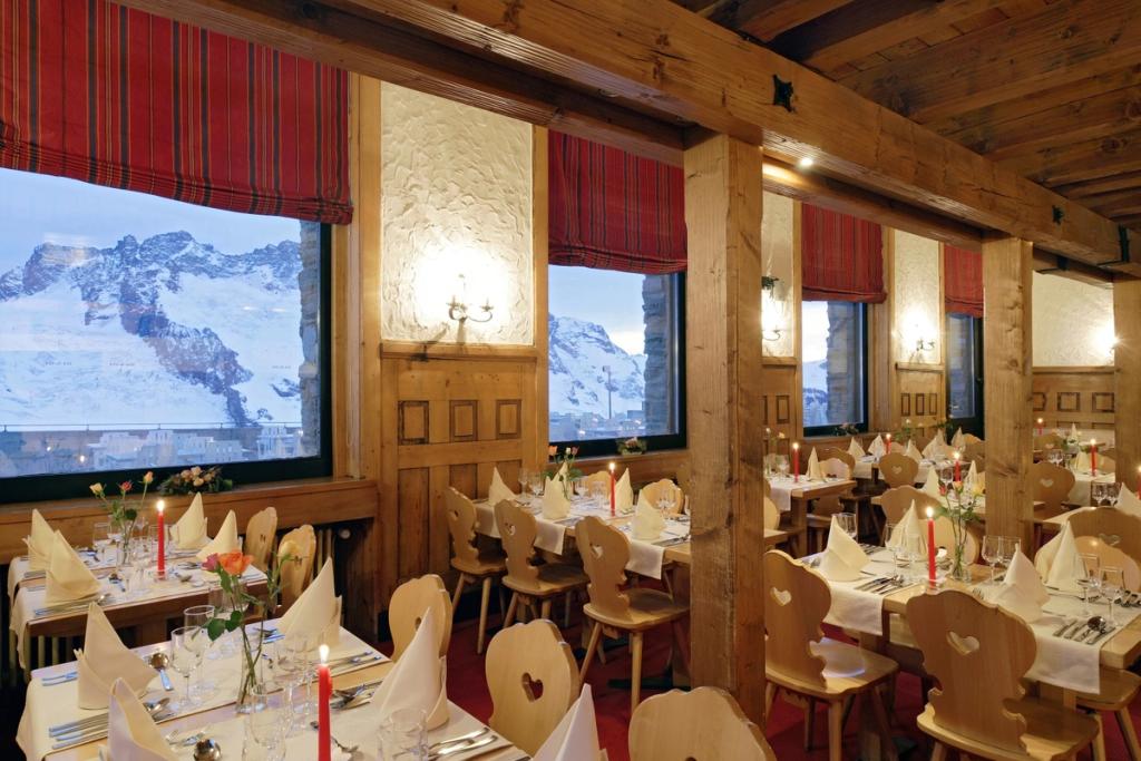 A wooden Alpine-style restaurant with candles and windows onto the snowy mountains