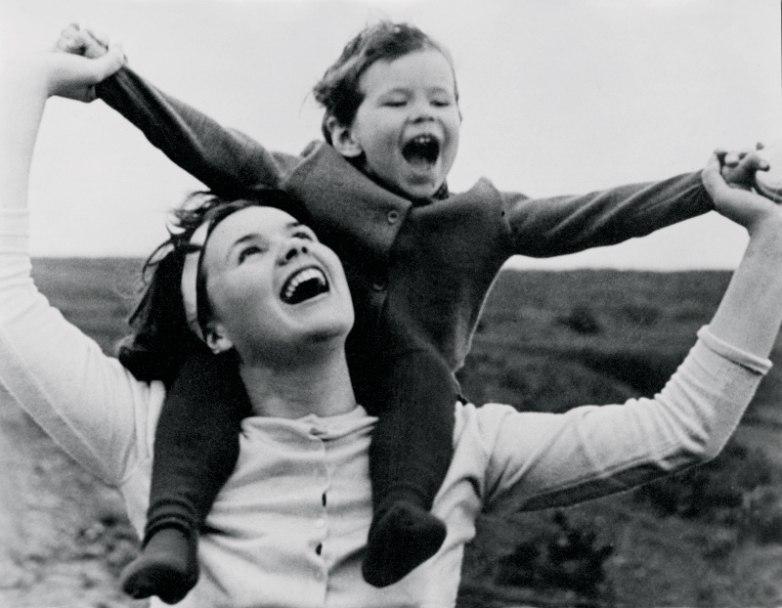 Two young female workers in aprons talk and laugh, the background blurred by motion