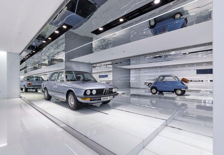 Серебристый седан BMW на подиуме рядом с голубым микрокаром BMW Isetta в зеркальном зале