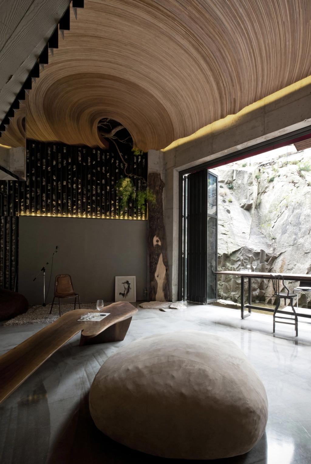 Interior with a spiral rattan ceiling, a concrete wall and a view onto the rock face through a sliding door