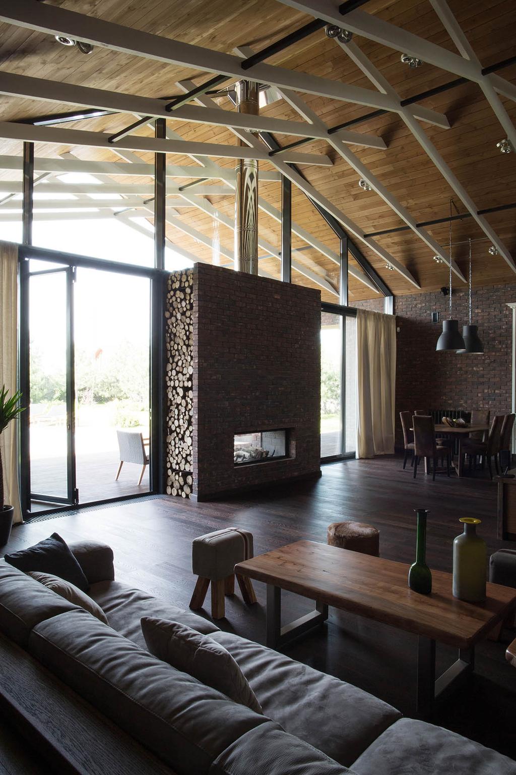 A double-height living room with a timber ceiling on white trusses and a brick fireplace with a log store