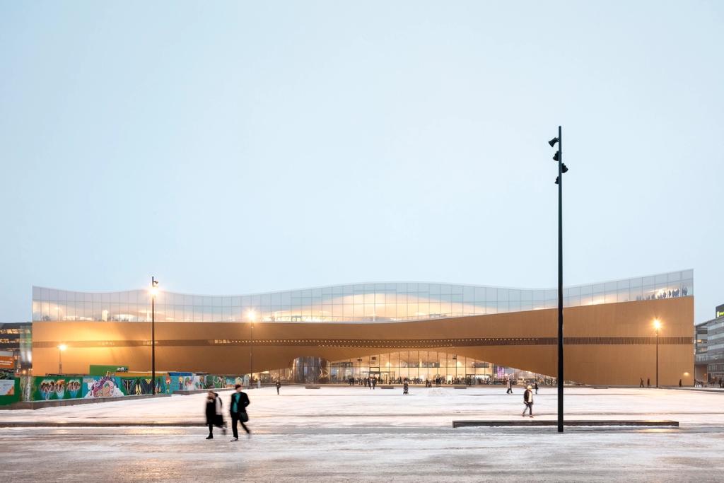 The glazed upper floor and undulating timber volume of Oodi library on the square at dusk