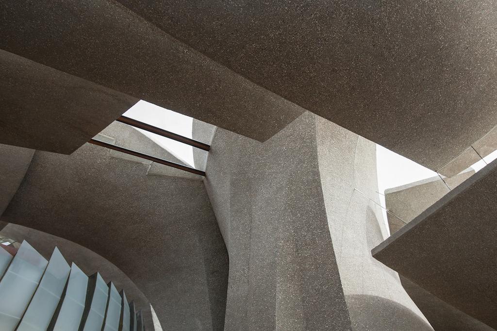 Interior of a house with concrete vaults, an embedded boulder, ivy and a copper fireplace