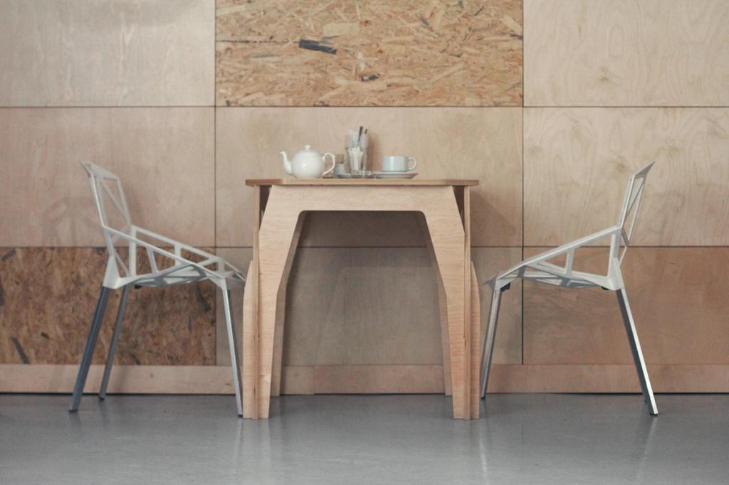 A plywood table and two metal chairs against a wall of OSB panels, designed by Lyosha Galkin