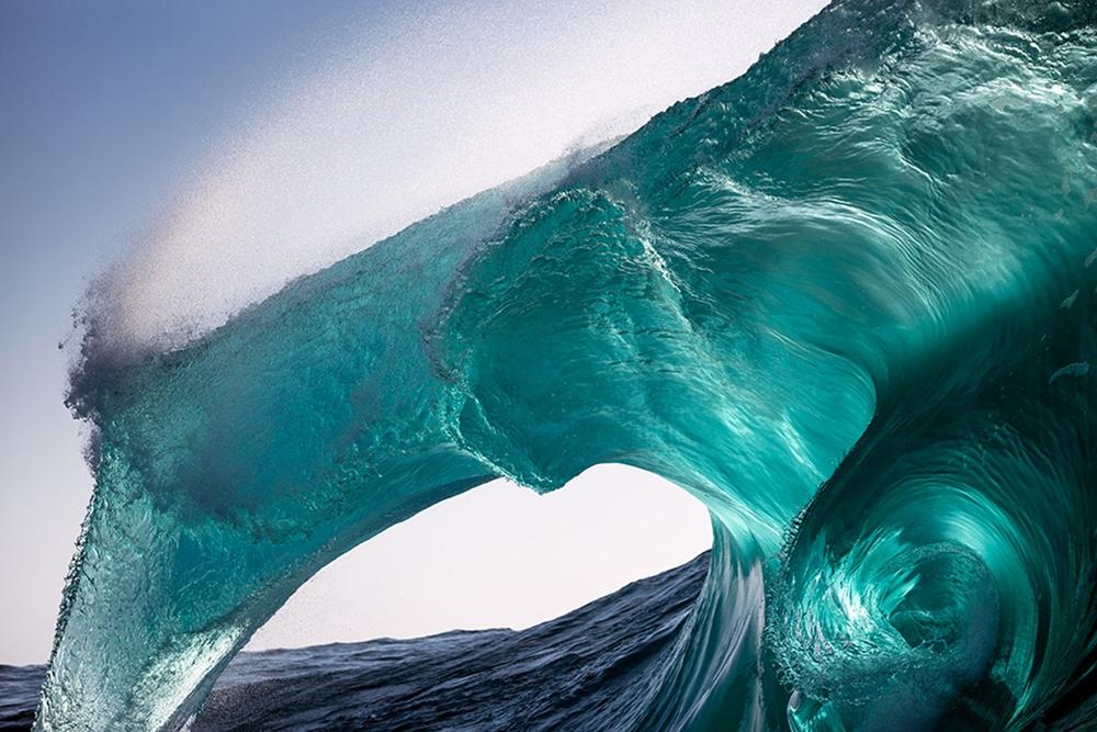 A translucent turquoise wave forming a water arch against a bright sky