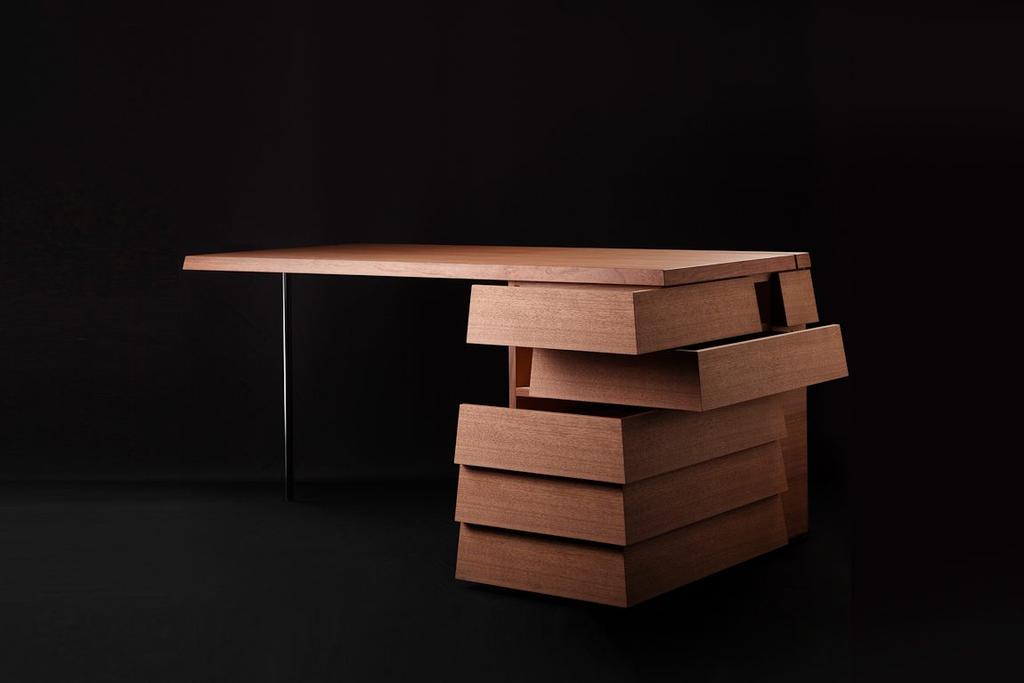 Wooden writing desk with offset stepped drawers against a dark background