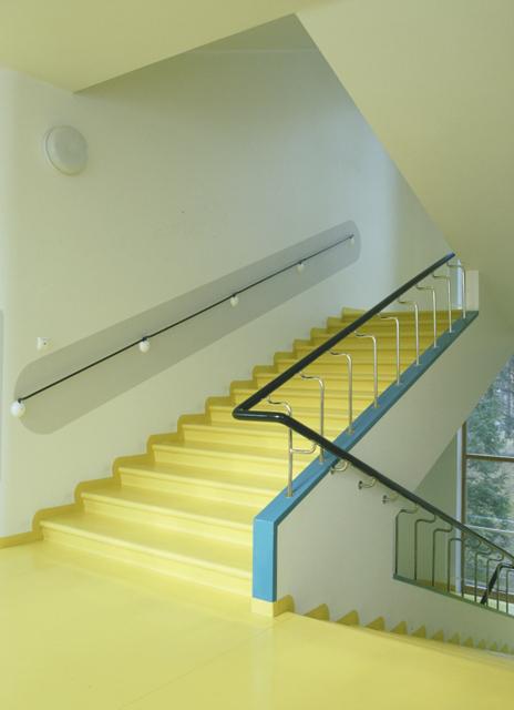 The yellow staircase of the Paimio Sanatorium, with a curved wall-mounted handrail and a blue accent
