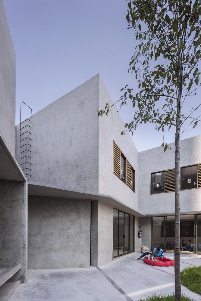 The grey concrete volume of Walden Dos School with its inner courtyard and a tree