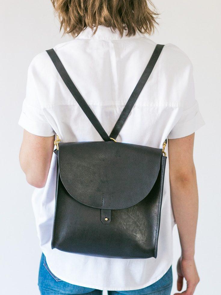 A black leather Tribe Alive backpack on the back of a woman in a white shirt