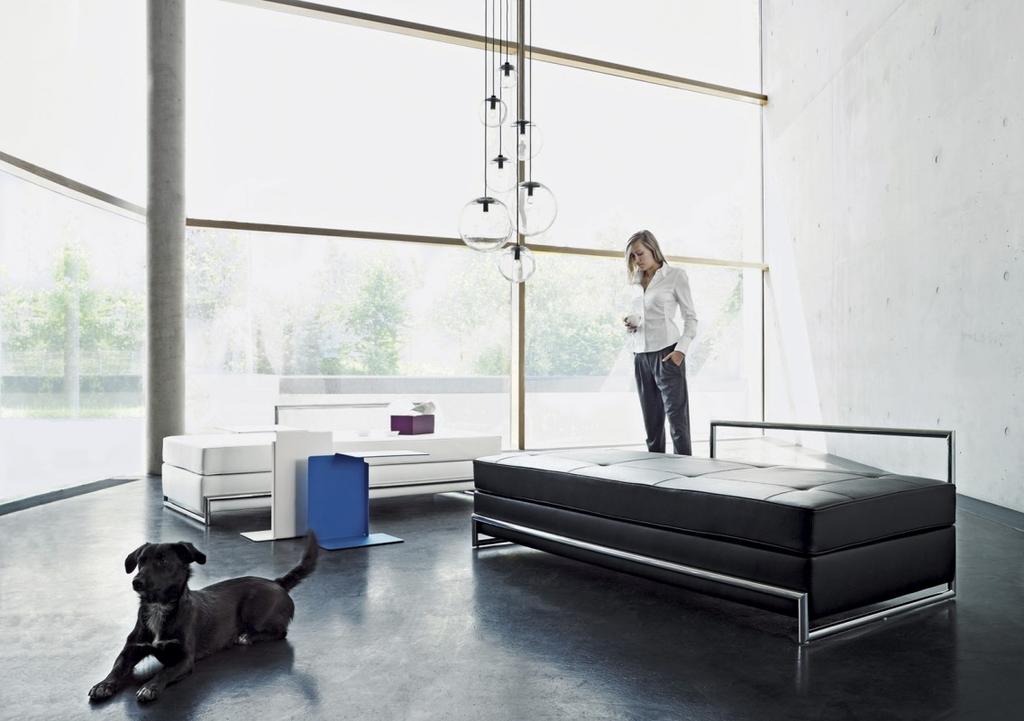 View through a glass wall: a white curved chaise longue, a rug and pendant glass light fixtures