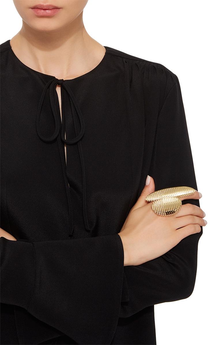 A gold ridged ring with a streamlined form on the finger of a model in a black dress