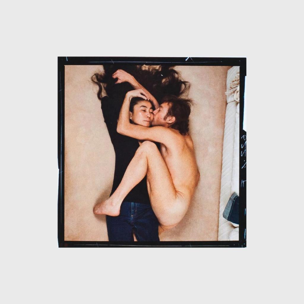 A naked John Lennon embracing a black-clad Yoko Ono as they lie on the floor