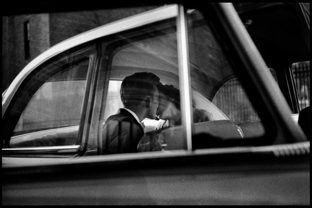 A couple kissing on the back seat of a car, photographed through the window