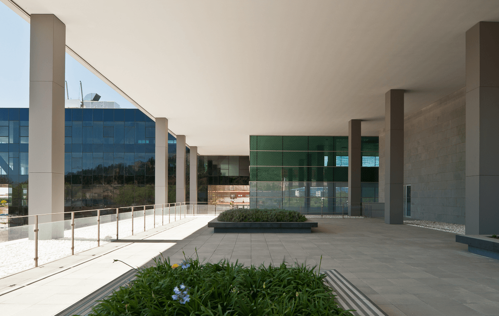 The drop-off area of the D38 office building beneath a canopied overhang on columns, with a landscaped green zone