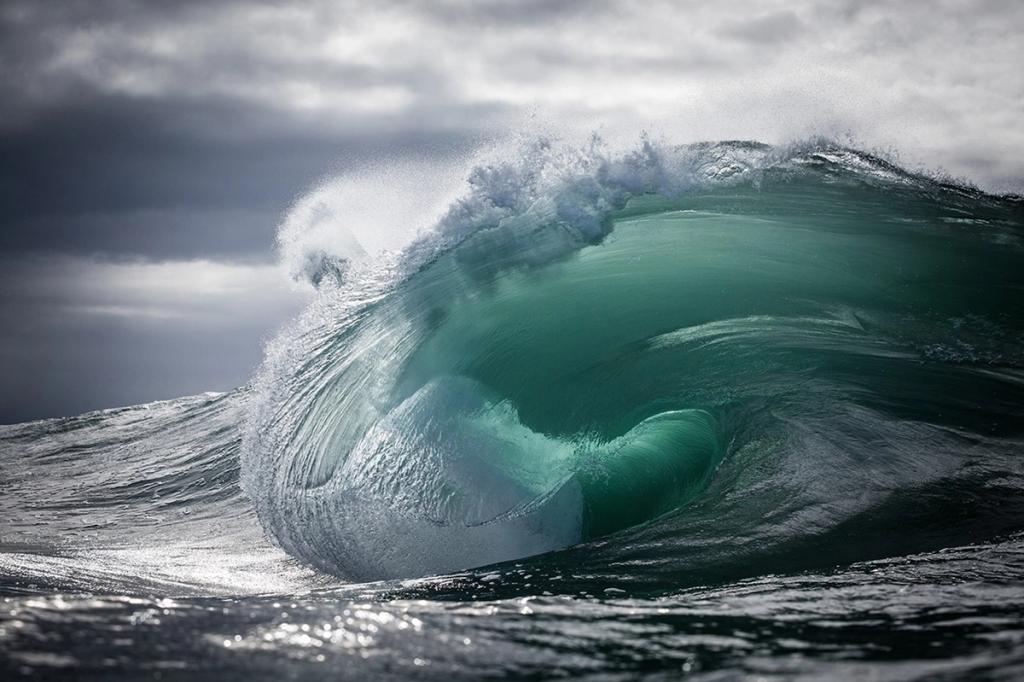 A green wave with a foamy crest against stormy grey clouds over the ocean