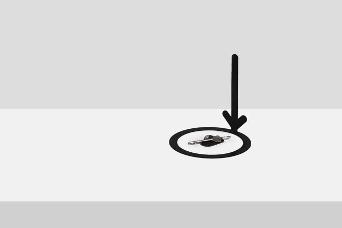 A minimalist key dish in the shape of a black arrow pointing to a bunch of keys, designed by Maxim Maximov