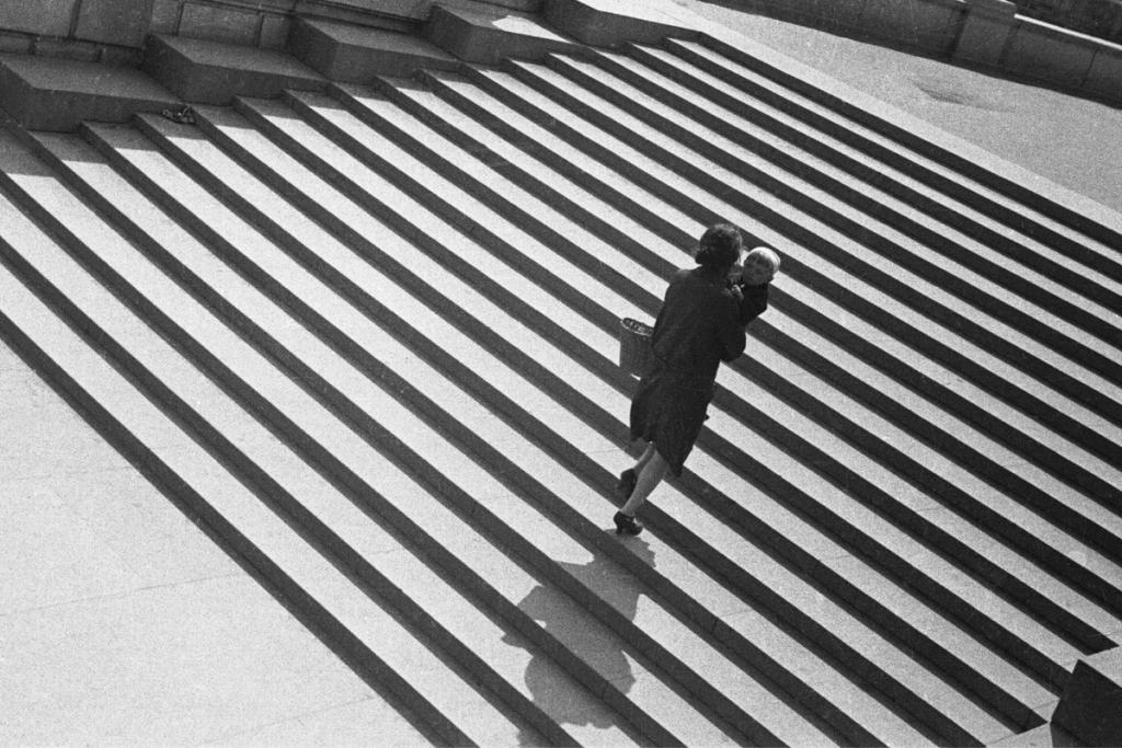 An overhead view of a stone staircase with stark diagonal shadows and a woman walking