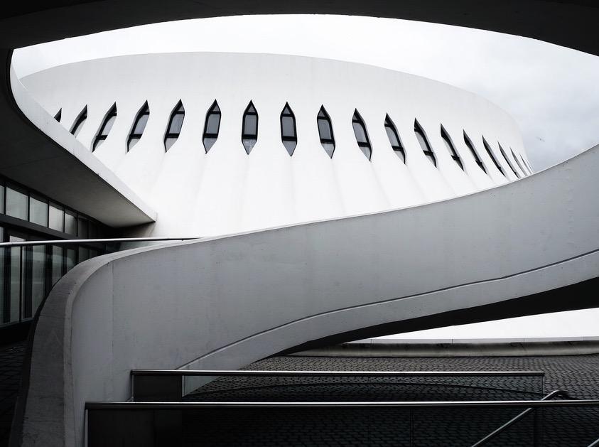 A curved white volume with a row of narrow slit windows and a ramp