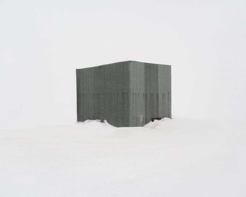 A grey concrete structure with no windows, half-submerged in snowdrifts