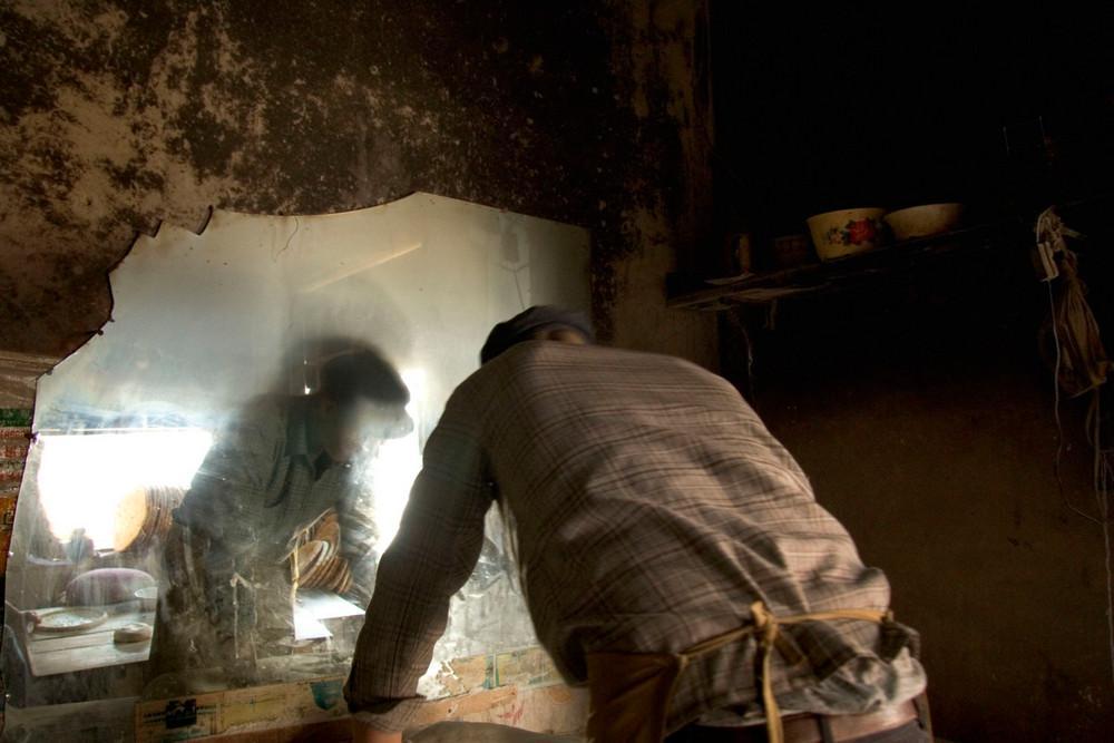 Two men by a cracked mirror in the half-light of a village house
