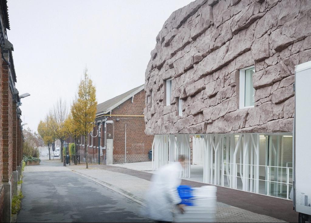 The volume of The Roc School, clad in pink stone, beside a red-brick neighbourhood