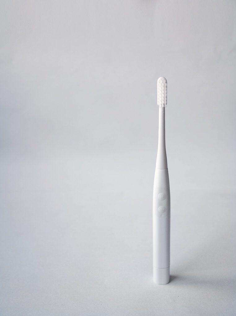 A white electric toothbrush standing upright against a light grey background