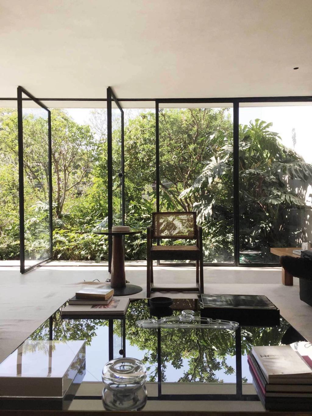 A living room with a mirrored table and pivoting glass walls opening onto a green garden