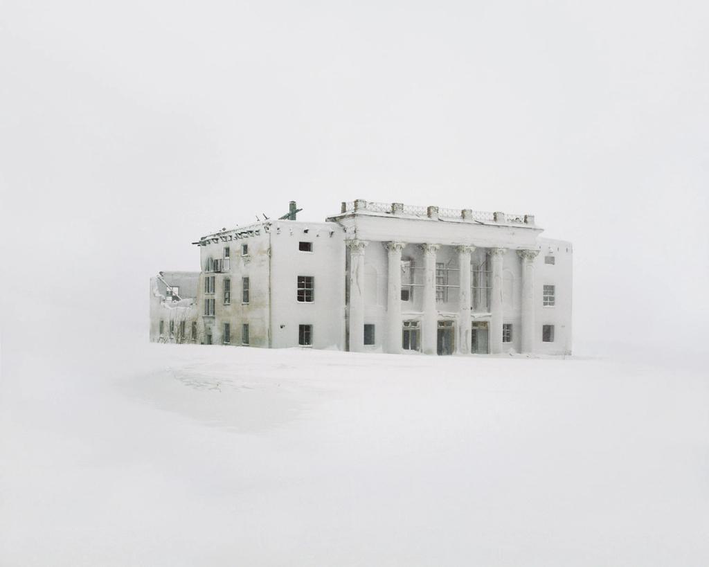 An abandoned colonnaded building with a portico, buried in snow within a white expanse