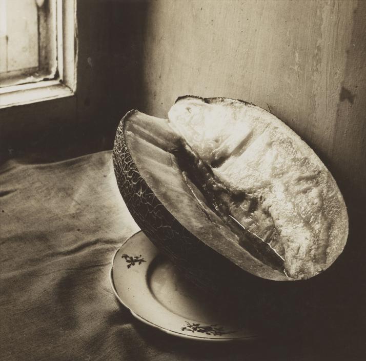 A still life with a sliced melon on a plate by a window in soft light