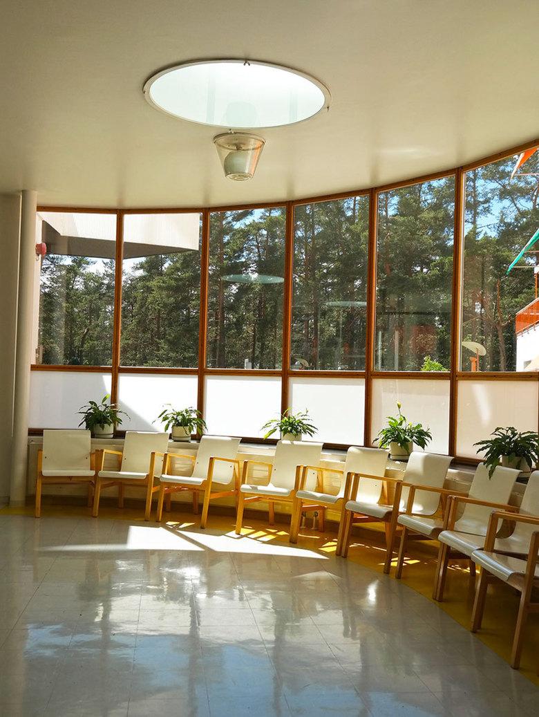 The curved solarium of the Paimio Sanatorium, with windows overlooking a pine forest and white armchairs
