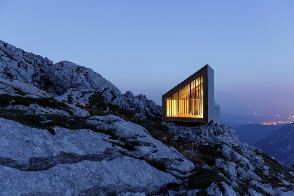 Убежище Alpine Shelter Skuta на скальном уступе в сумерках, светящиеся панорамные окна над Люблянской котловиной