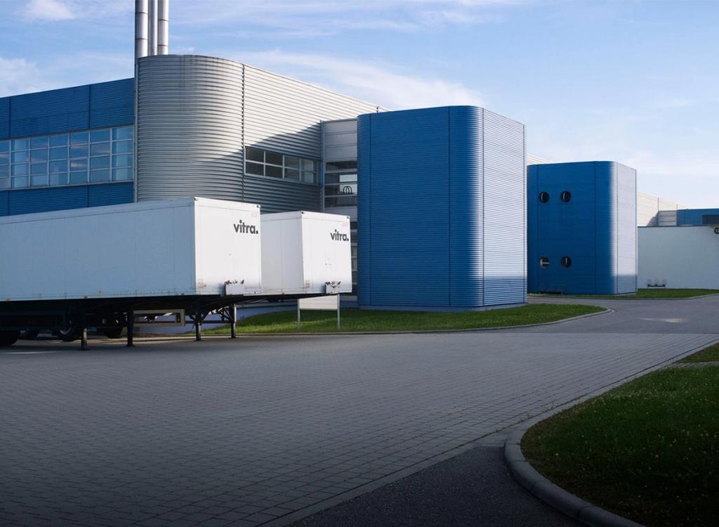 Синие производственные корпуса Vitra и белые грузовые полуприцепы у завода Гримшоу
