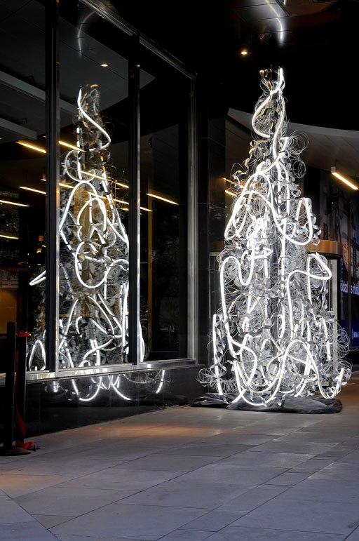 Two neon-tube trees and their reflections in a building's glazed frontage