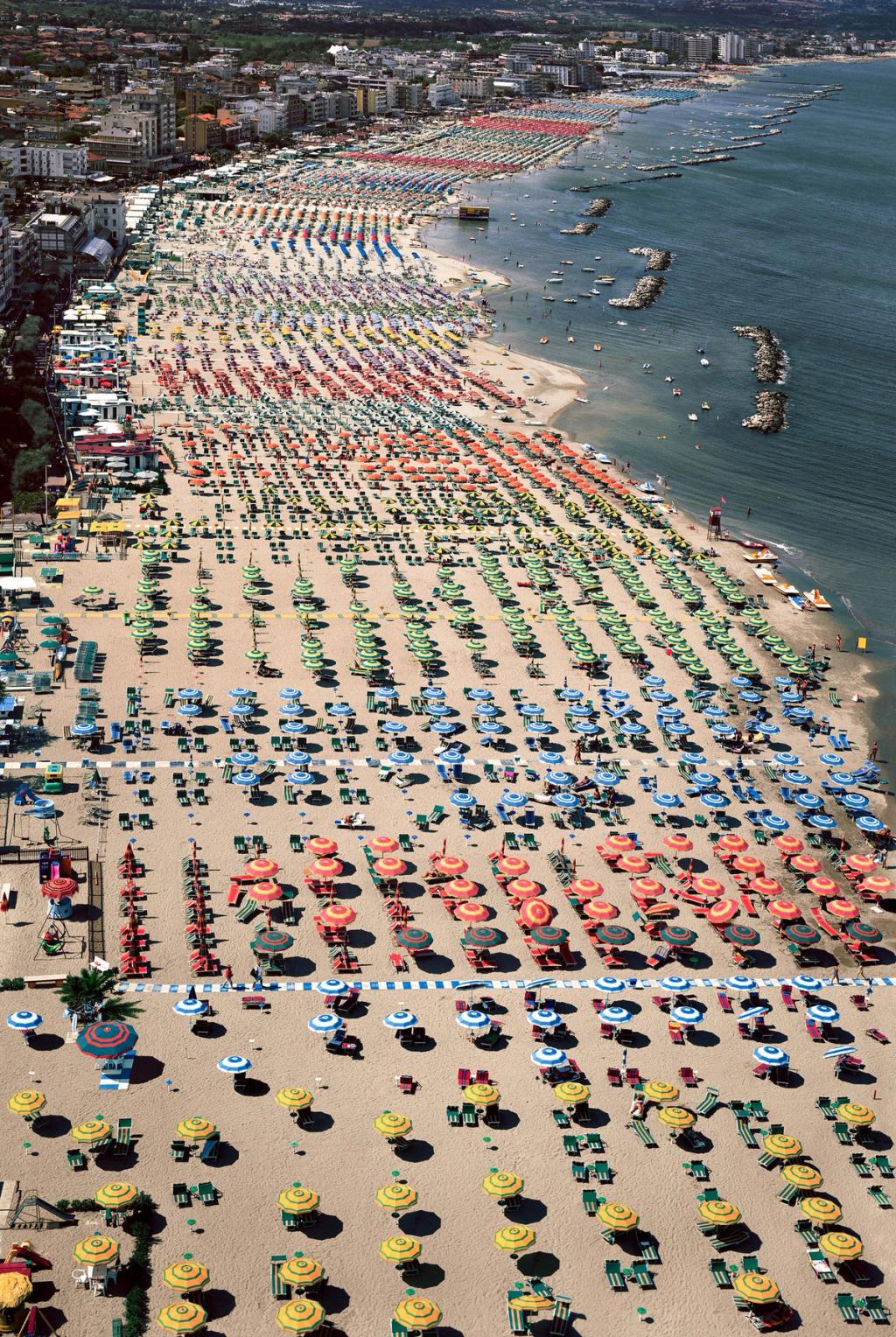 A beach from above: endless rows of colourful umbrellas and sun loungers along the water's edge
