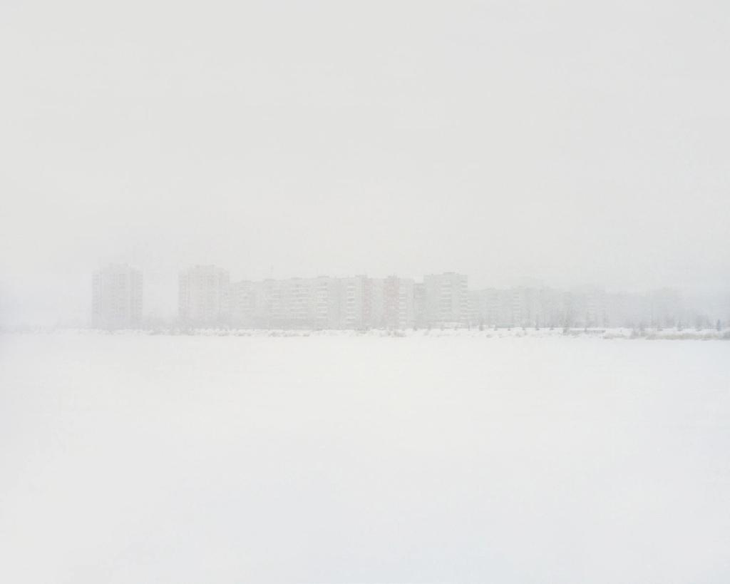 Multi-storey prefabricated residential blocks in the distance, dissolving into a snowy haze