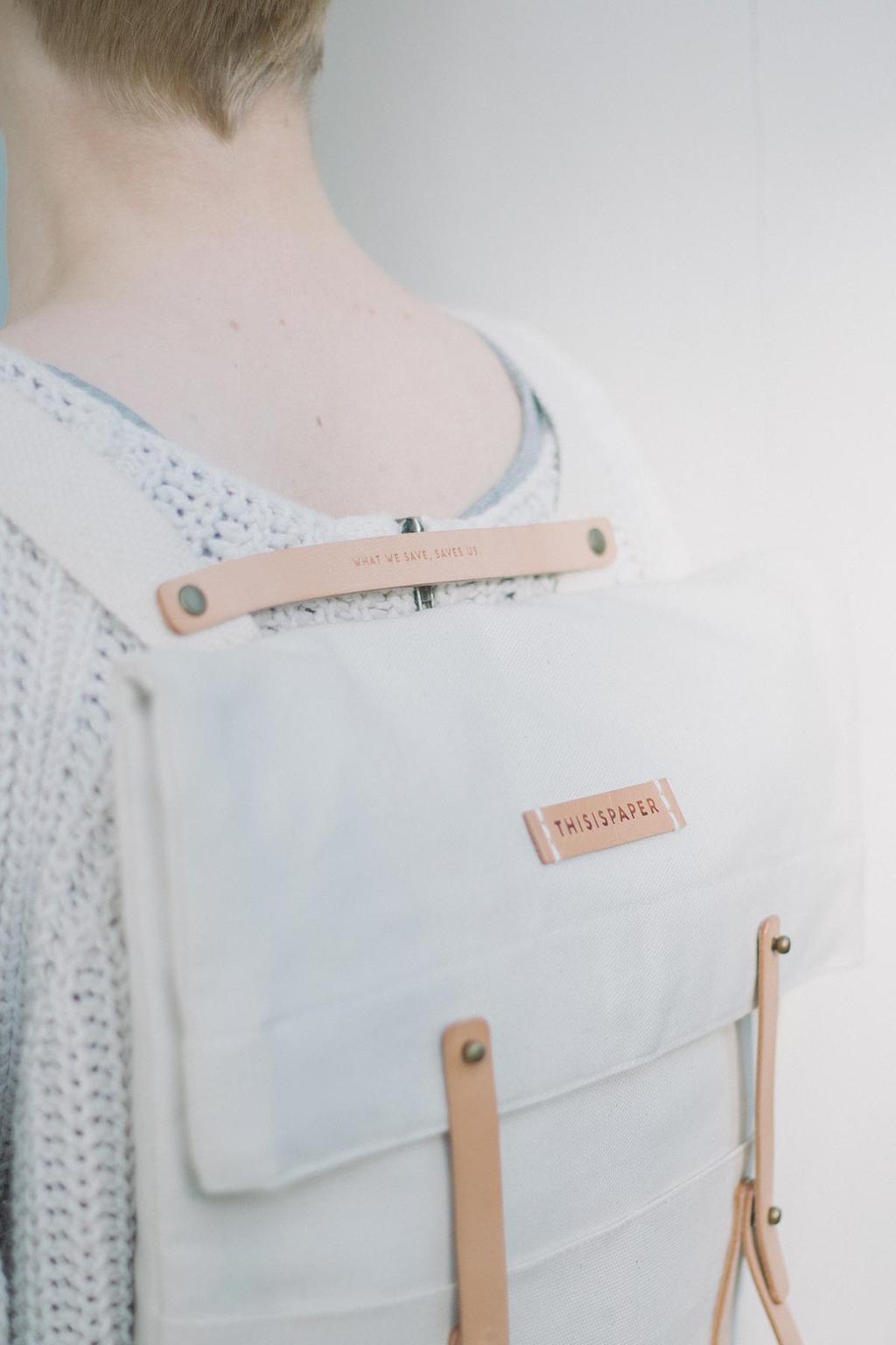 A white canvas Thisispaper backpack with leather straps, seen from behind on a woman