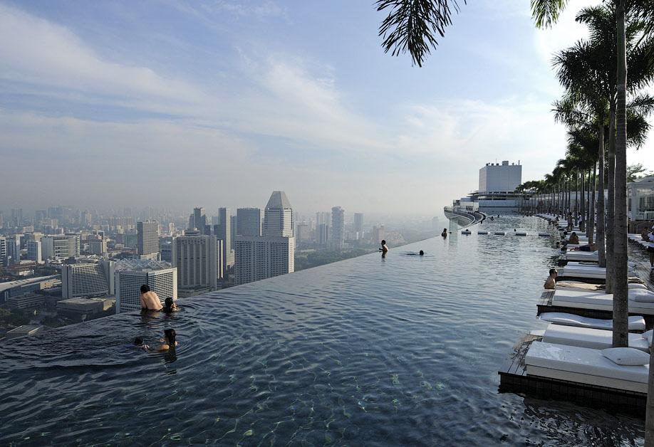 Бесконечный бассейн Marina Bay Sands с шезлонгами и панорамой Сингапура в дымке