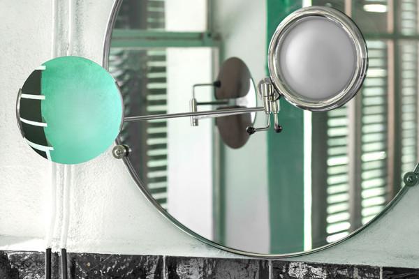 A round wall mirror with a pivoting magnifying glass above the bathroom sink