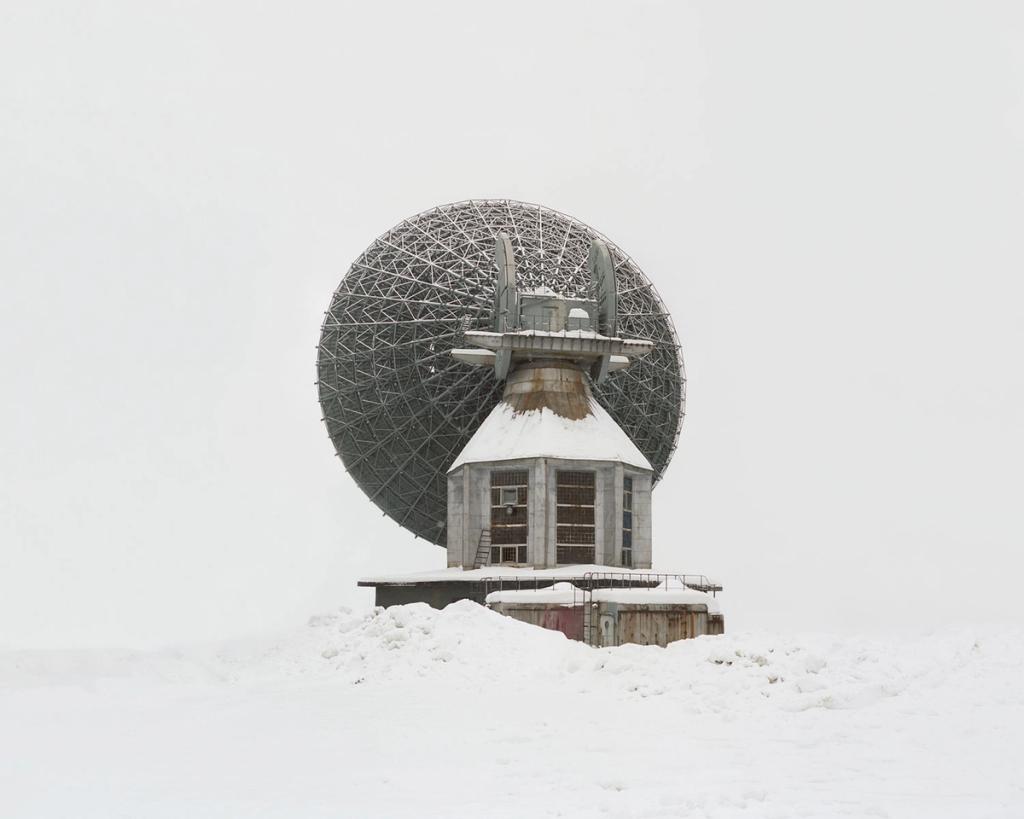 An abandoned deep-space communication antenna with a lattice dish, buried in snow