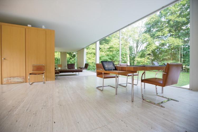 Light-filled interior of the Farnsworth House with panoramic glazing, a view of the forest, and Brno chairs