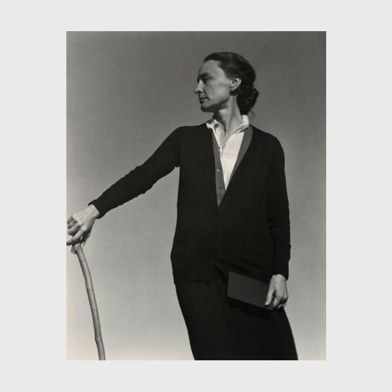 A black-and-white Stieglitz portrait: O'Keeffe standing, resting her hand on a cane