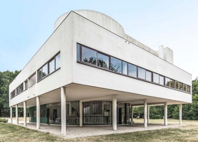 The white volume of Villa Savoye raised on pilotis, with ribbon windows and surrounded by trees