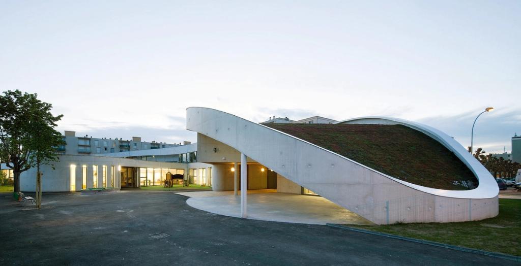 Ecole Jean-Moulin school: a white curved volume with a green roof at dusk