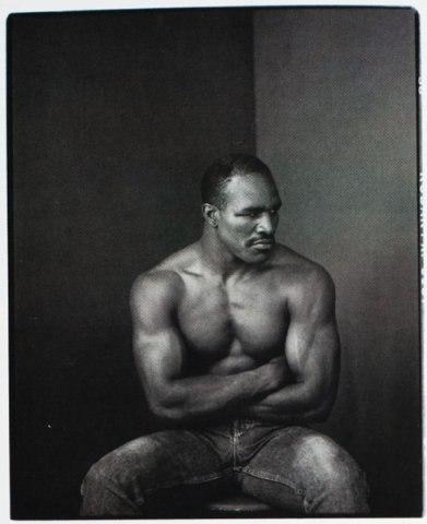 Portrait of a muscular man with crossed arms in the corner of a studio, by Annie Leibovitz